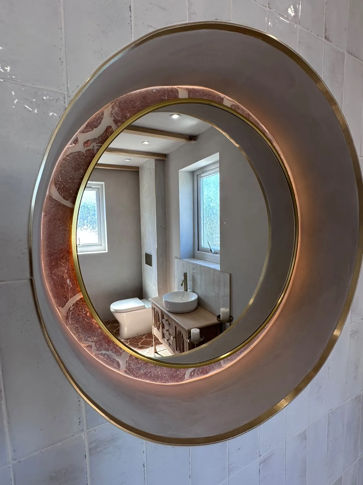 Backlit round mirror with brass trim and terracotta tile detail fitted in a bathroom renovation