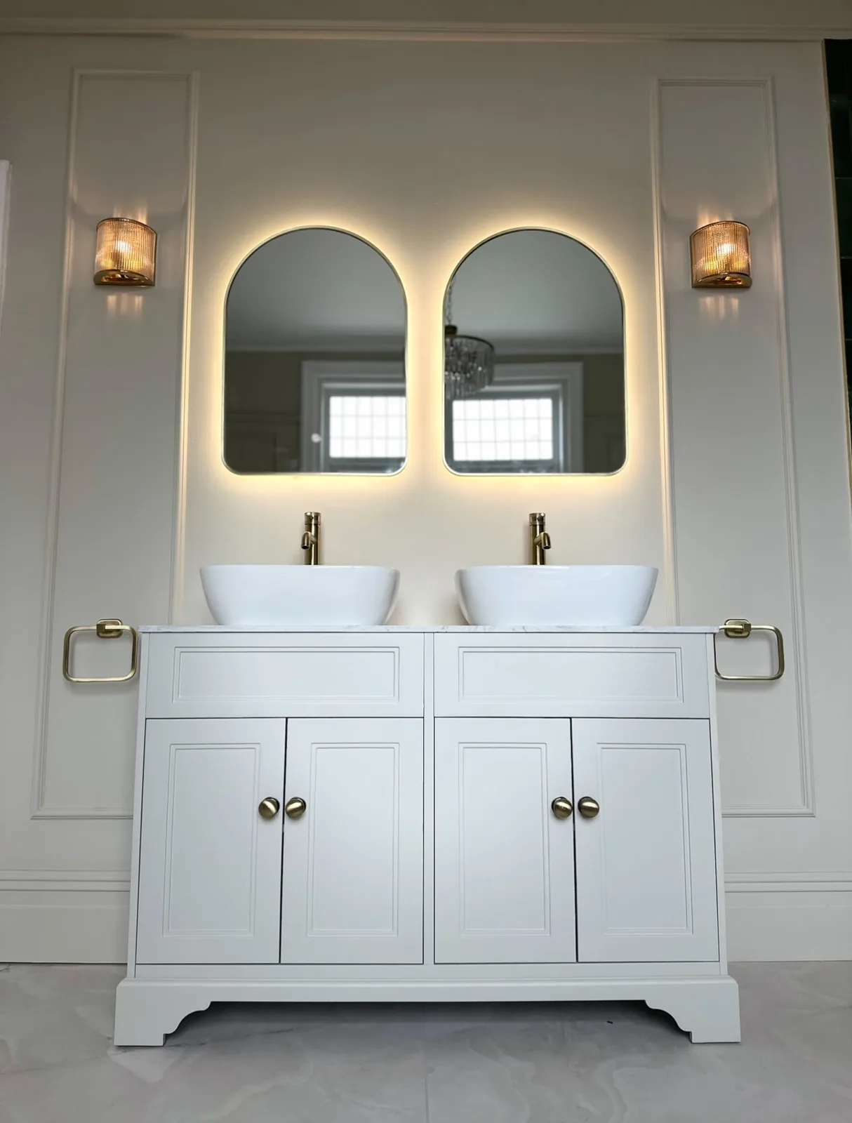 Double vanity unit with brass taps and backlit arched mirrors fitted during a bathroom renovation
