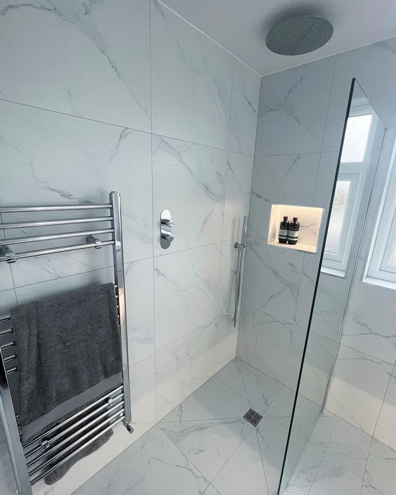 Wet room walk-in shower with marble-effect tiling, chrome rainfall shower and illuminated recessed storage niche