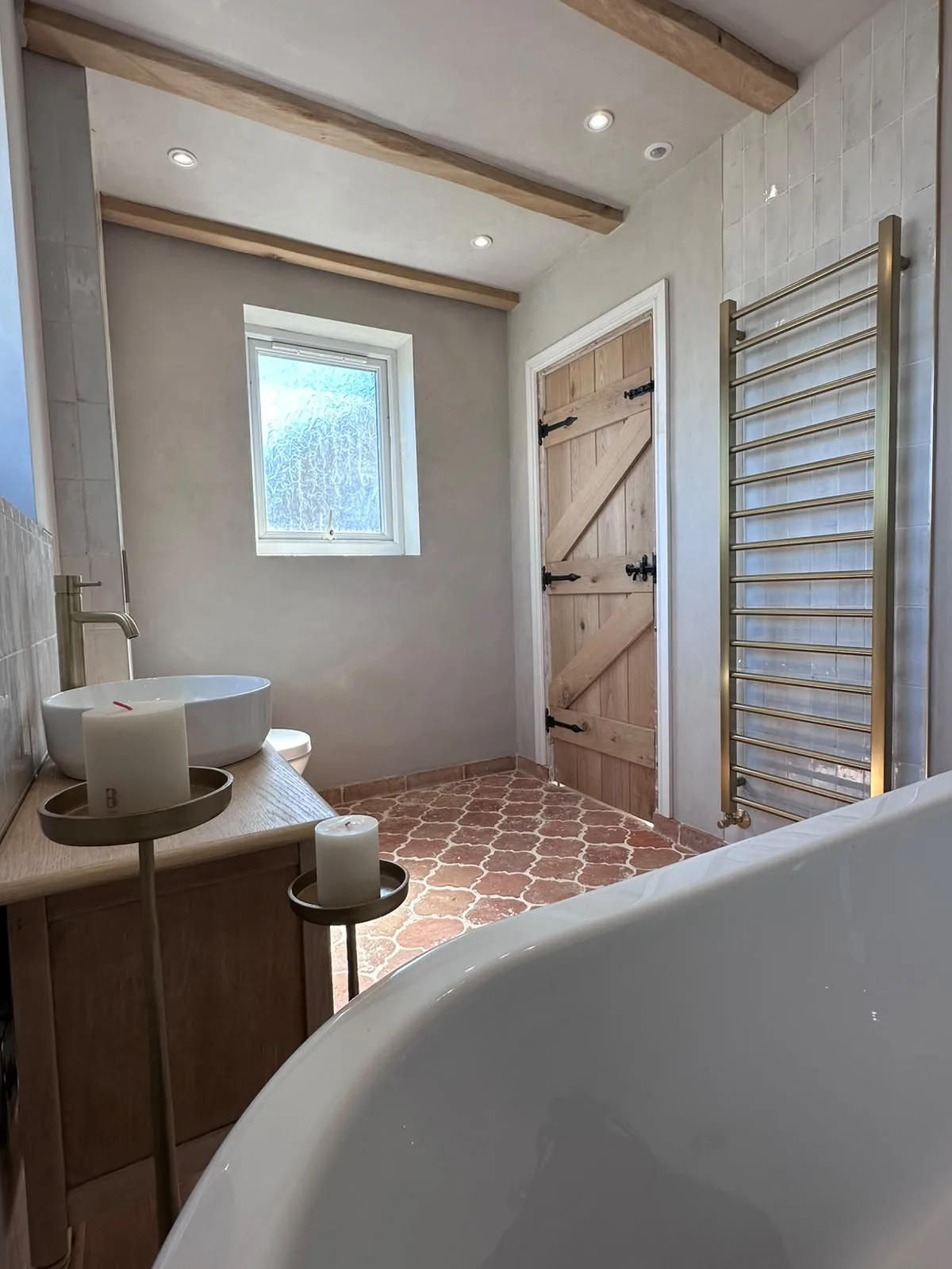 Bathroom renovation with oak beams, brass ladder towel radiator, oak plank door and terracotta floor tiles