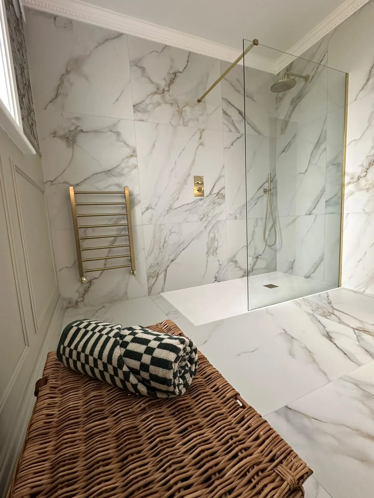 Walk-in wet room shower with marble-effect large format tiles, brass rainfall shower head and matching towel radiator